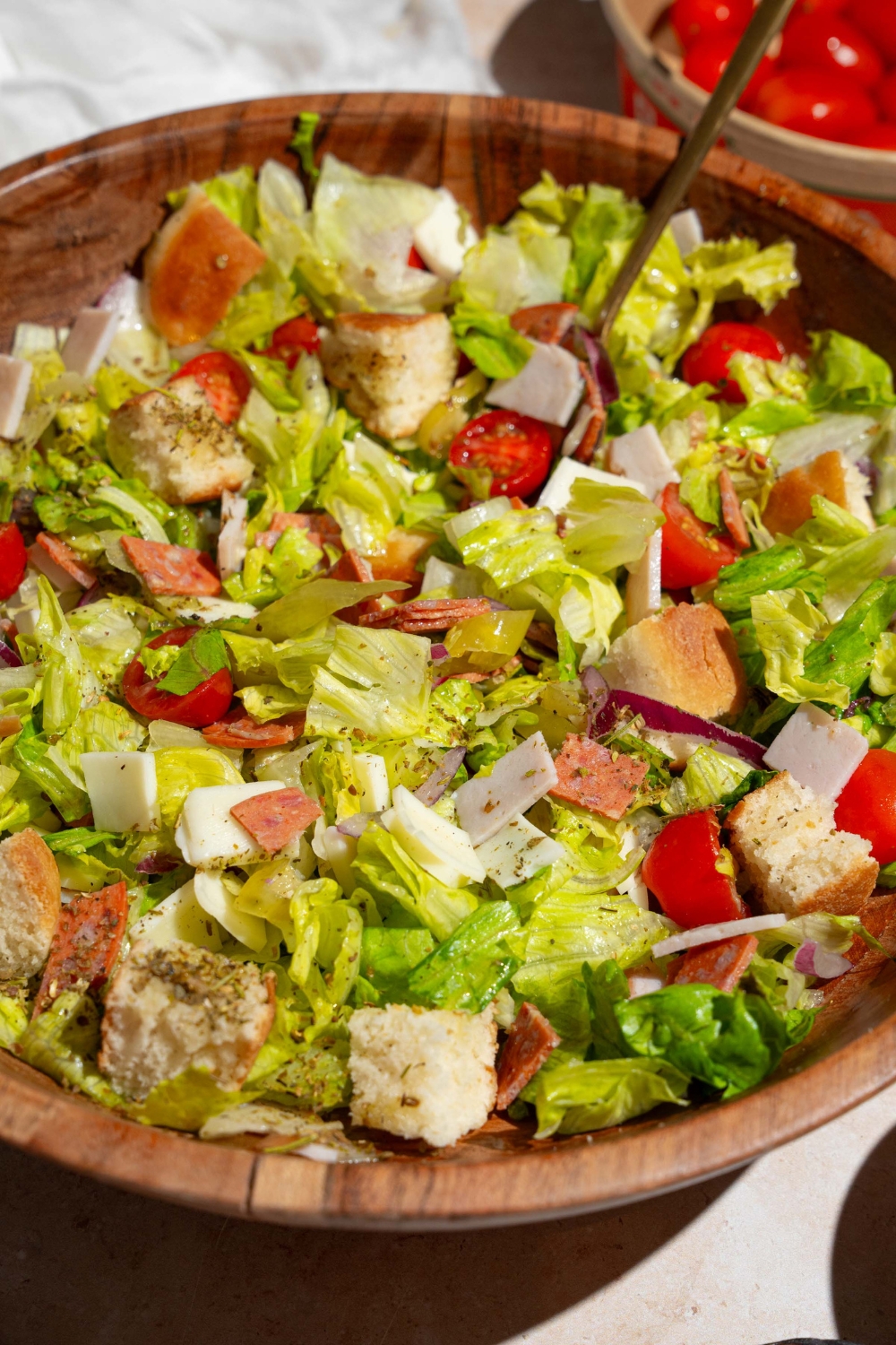 A wooden salad bowl of copycat Jersey Mike's sub in a tub including mixed lettuce, tomatoes, provolone cheese, diced meats, and bread croutons. There is a fork in the salad.