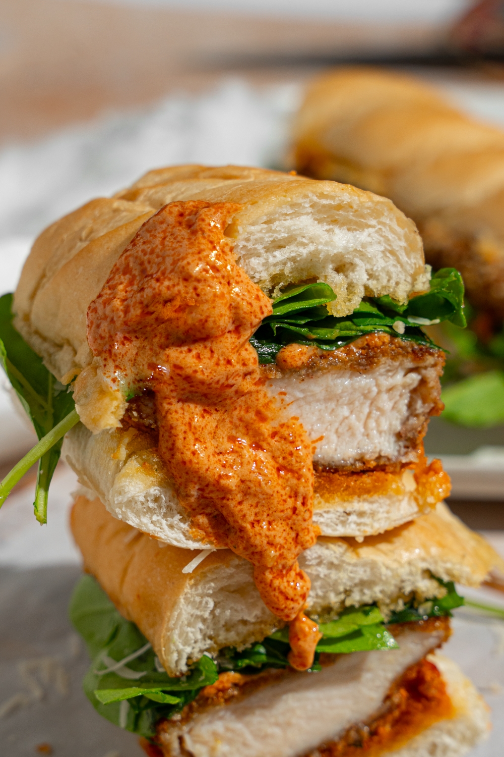 Two halves of a chicken cutlet sandwich stacked on top of one another with tomato cream sauce poured over the sandwich. The sandwich is on a wooden board lined with parchment paper.