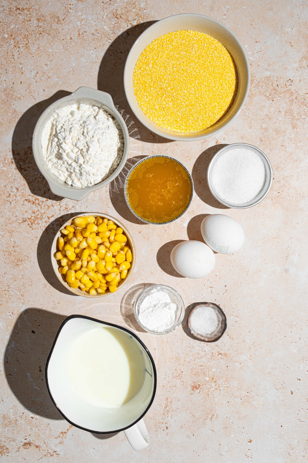An overhead shot of several bowls in various sizes containing ingredients to make Fat Daddy's cornbread including cornmeal, flour, baking powder, sugar, buttermilk, corn kernels, and butter.