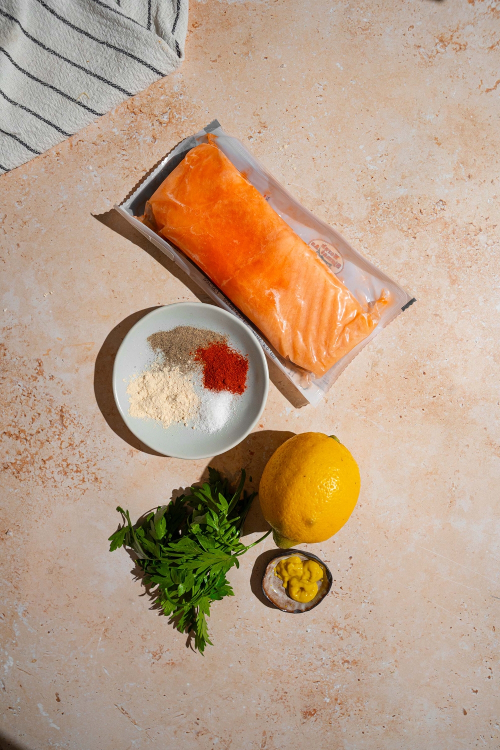 An overhead shot of ingredients to make frozen air fryer salmon including frozen salmon, lemon, fresh parsley, dijon mustard, and seasonings.