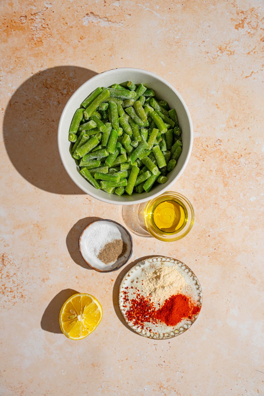 An overhead shot of ingredients to make sautéed frozen green beans including frozen green beans, lemon, oil, salt, pepper, and seasonings.