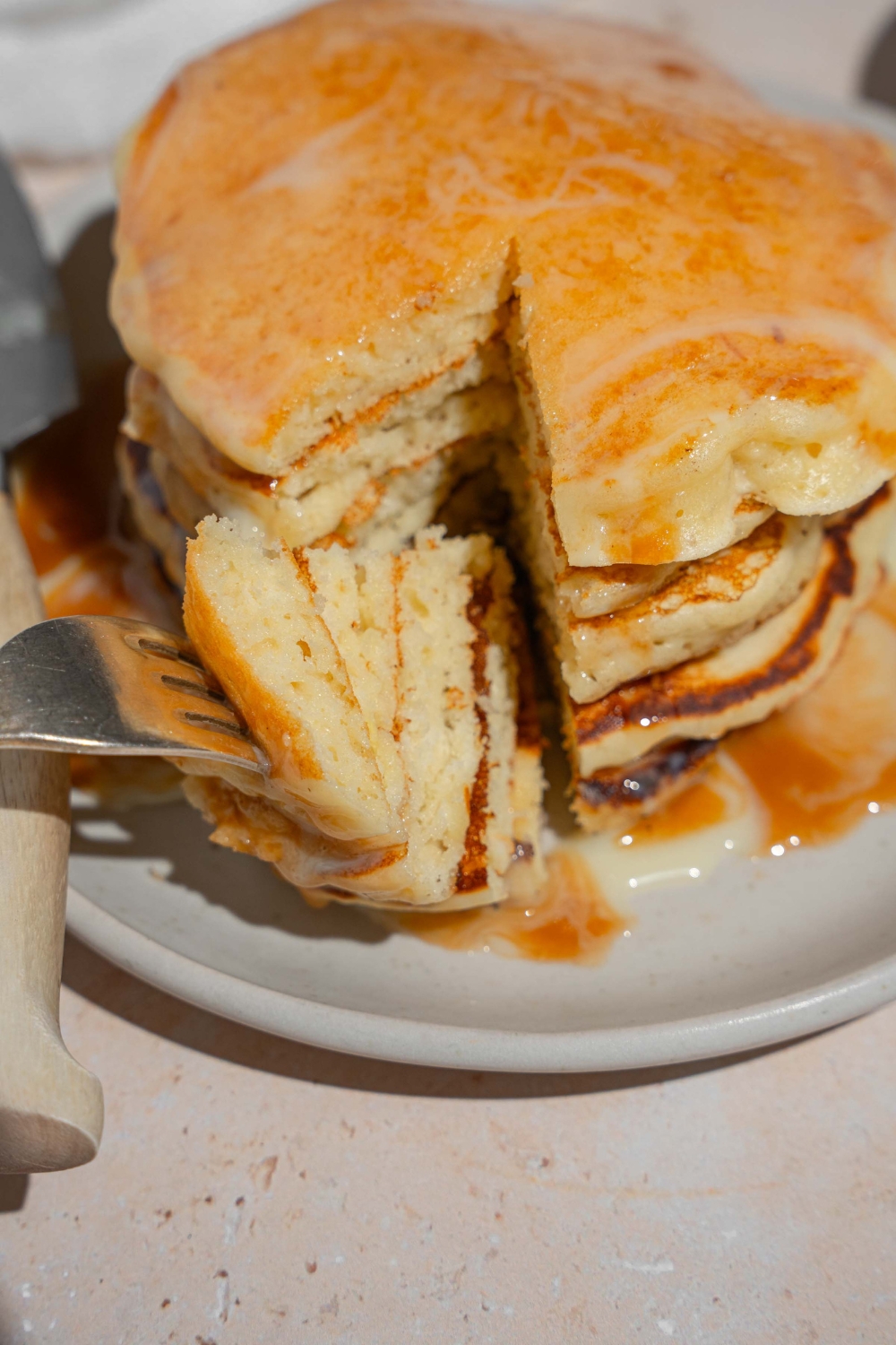 A stack of tres leches pancakes on a white plate with a fork taking a bite from the stack.