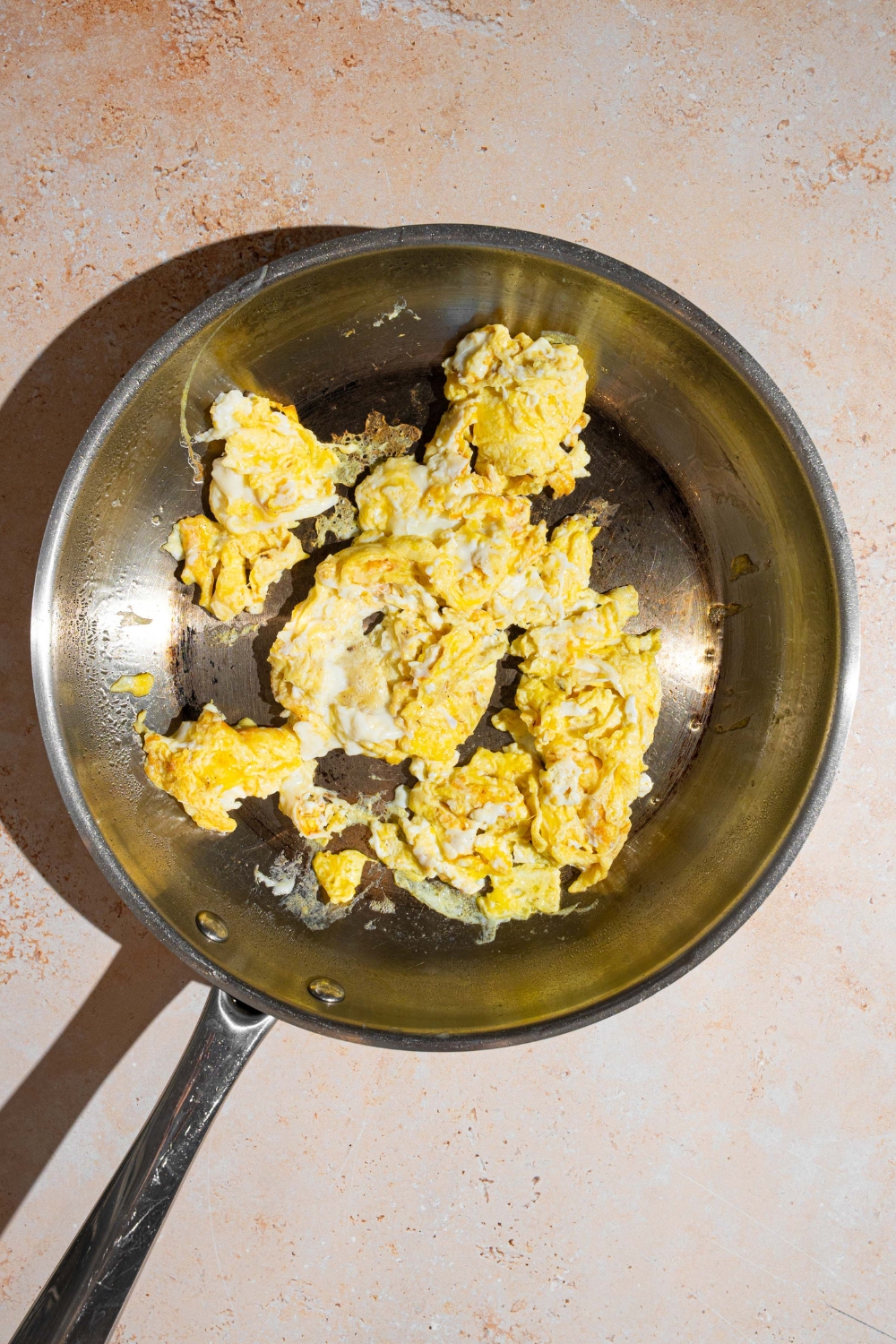 A skillet with scrambled eggs. The skillet is on a tan counter.