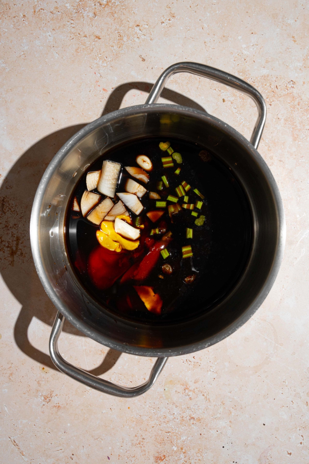 A stock pot with ingredients to make homemade A1 steak sauce including balsamic vinegar, water, worcestershire sauce, dijon mustard, raisins, and seasonings. The pot is on a tan counter.