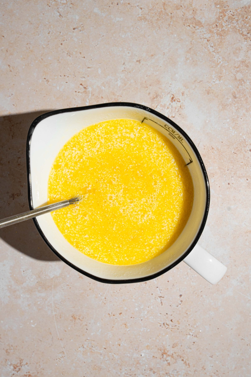 A spoon stirring wet ingredients to make cornbread. The mixture is in a ceramic bowl. The bowl is on a tan counter.