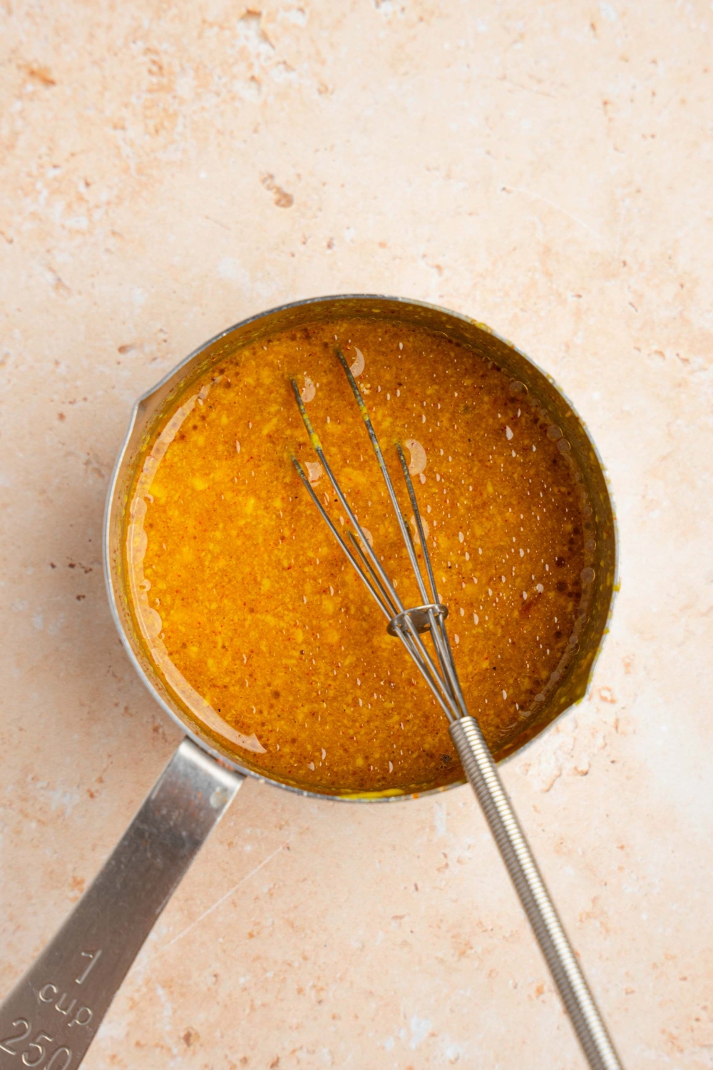 A small saucepan with a whisk mixing McDonald's golden sauce. The pot is on a tan counter.