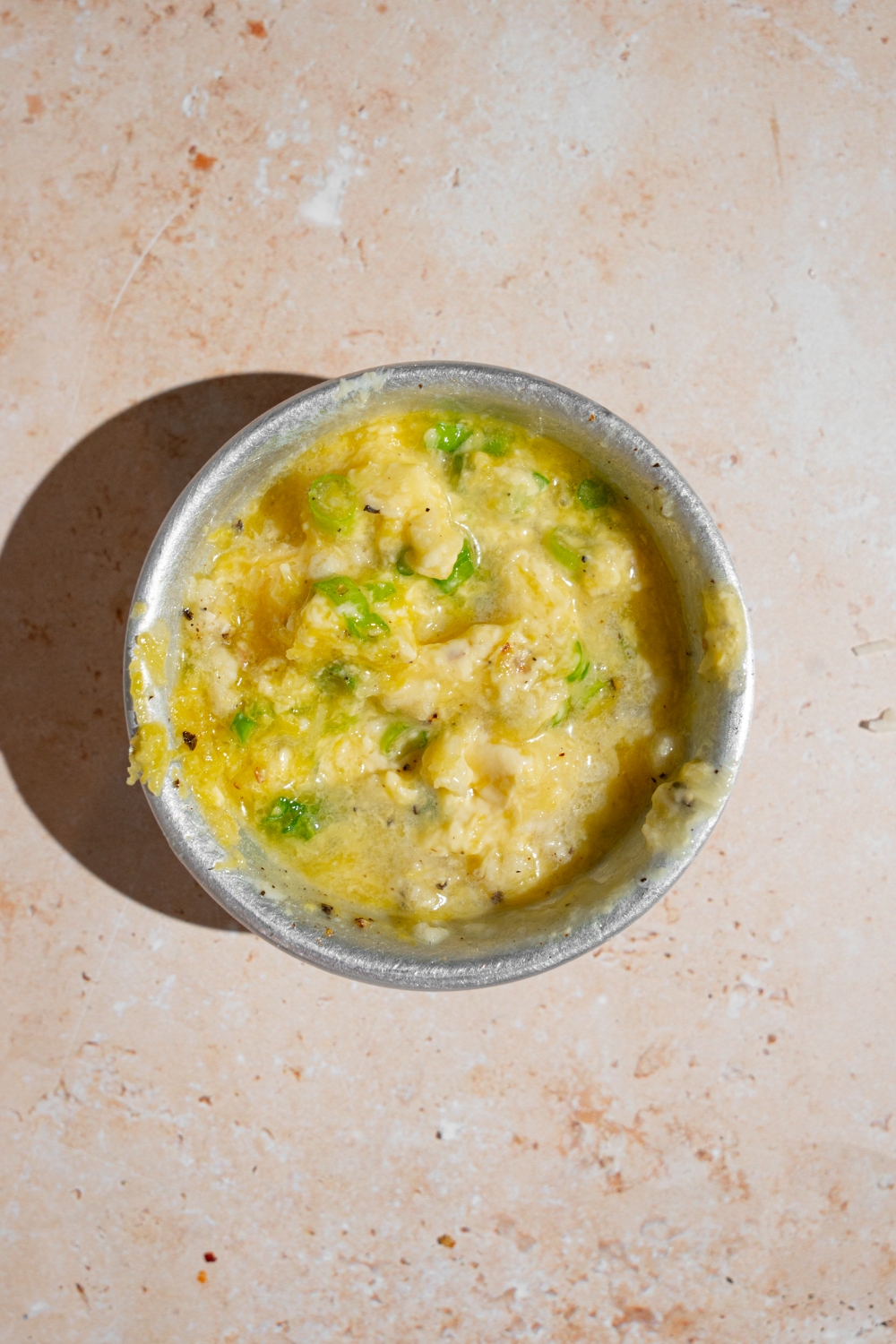 A small bowl with ingredients to make lemon garlic sauce including butter, chives, garlic, lemon, and seasonings. The bowl is on a tan counter.