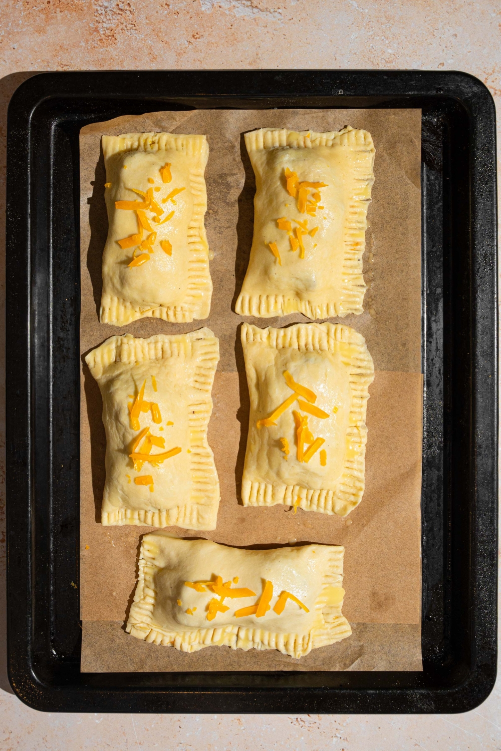 A baking sheet lined with parchment paper with five uncooked breakfast hand pies. The sheet is on a tan counter.