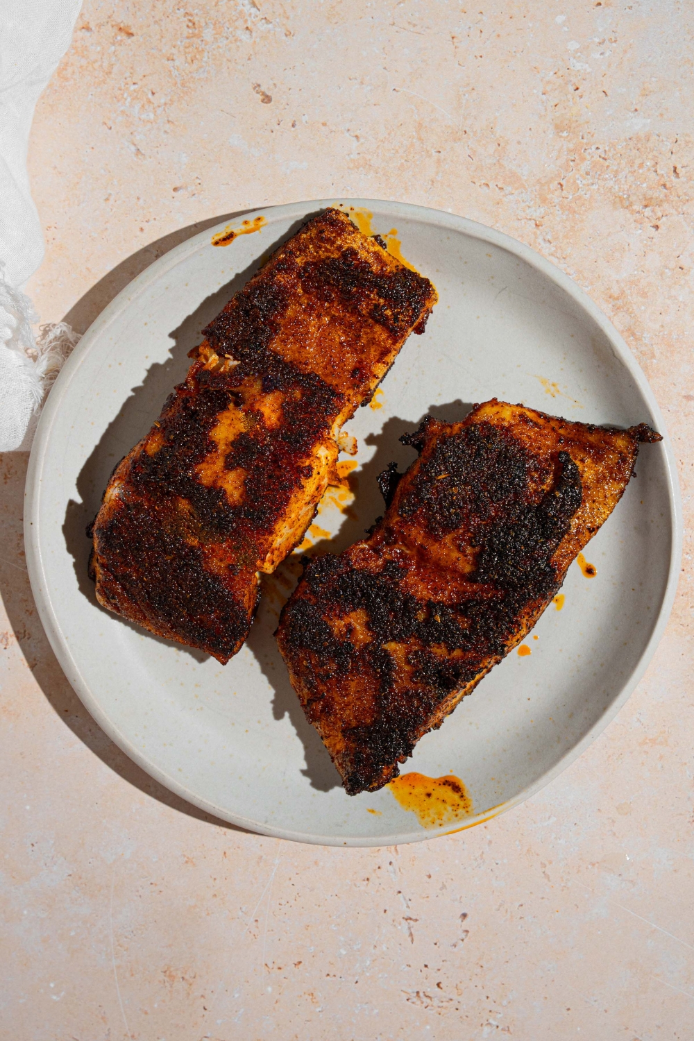 A white plate with two blackened grouper filets. The plate is on a tan counter.