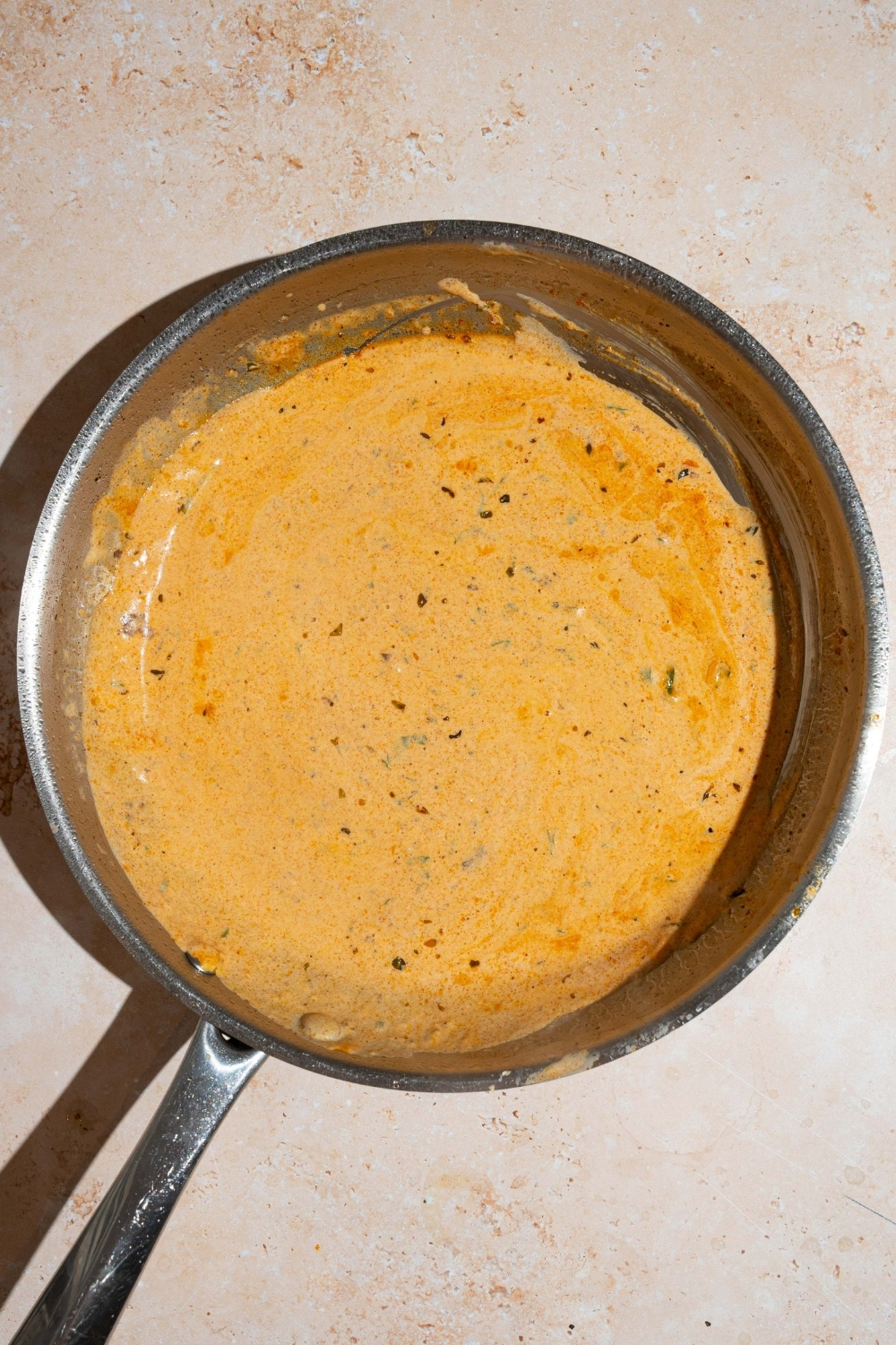 A skillet with cajun cream sauce. The skillet is on a tan counter.