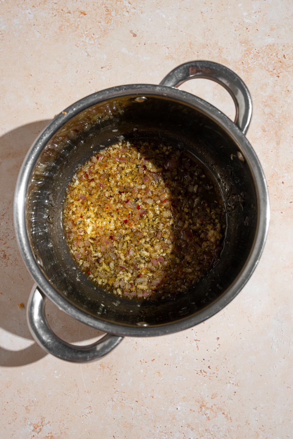 A stock pot with garlic, shallots, and spices cooking in boil and butter. The pot is on a tan counter.
