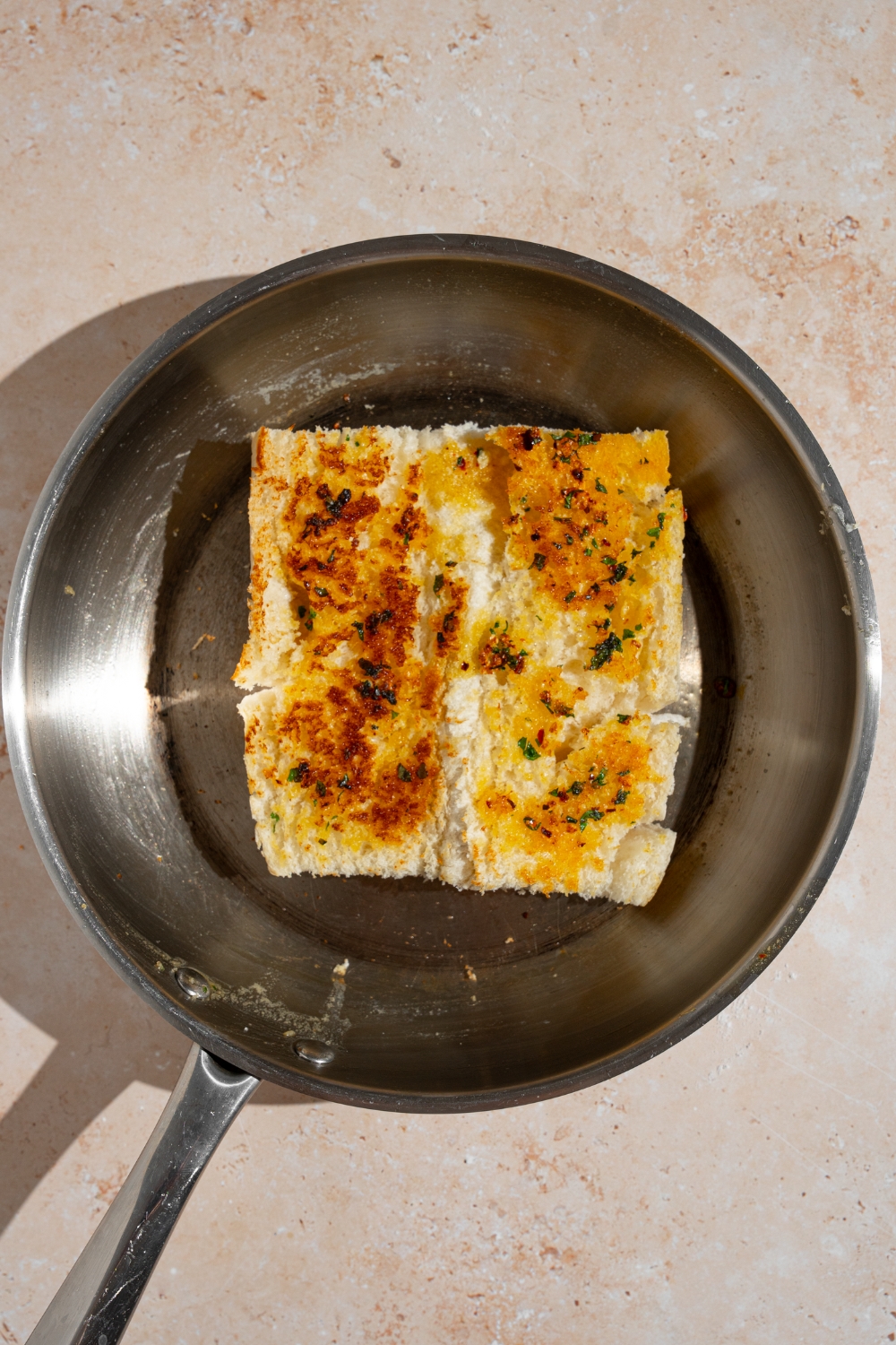 A skillet with an open loaf of sandwich bread toasted in garlic butter. The skillet is on a tan counter.