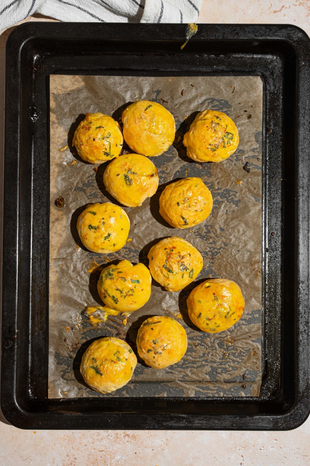 A baking sheet lined with parchment paper with baked garlic parmesan cheeseburger bites. The baking sheet is on a tan counter with a white striped napkin.