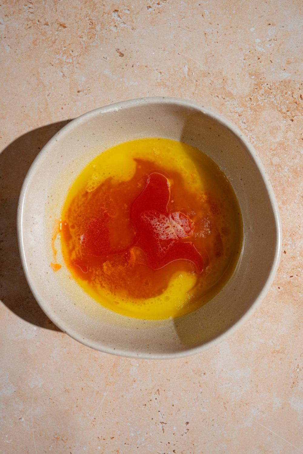 A white bowl with a hot honey mixture. The bowl is on a tan counter.
