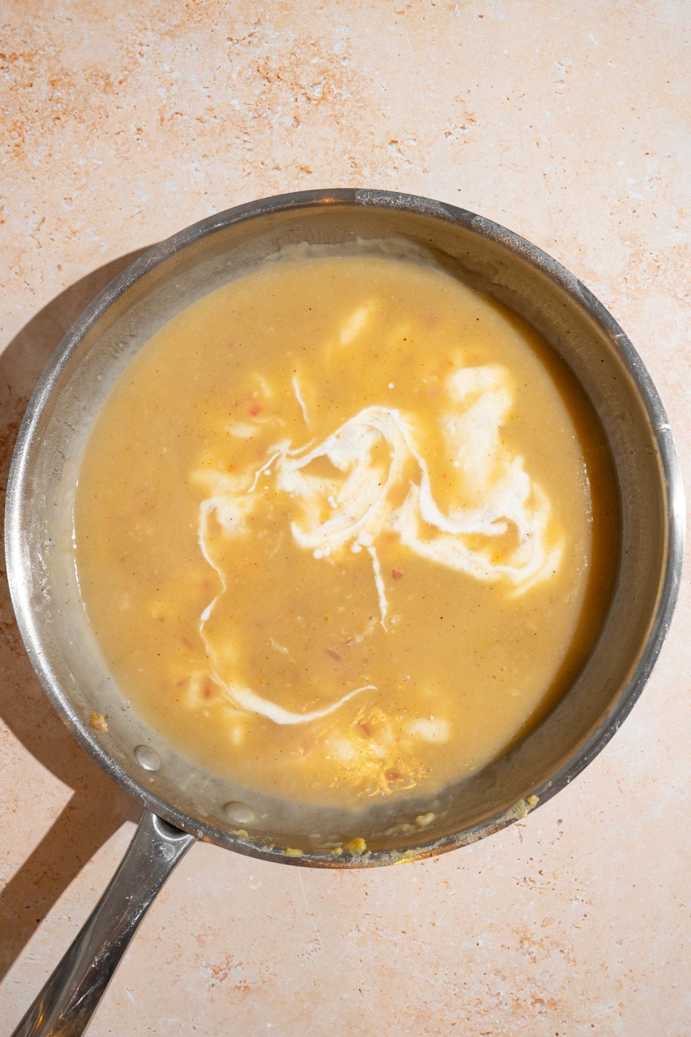 A skillet with Swedish meatball sauce base mixing with cream. The skillet is on a tan counter.