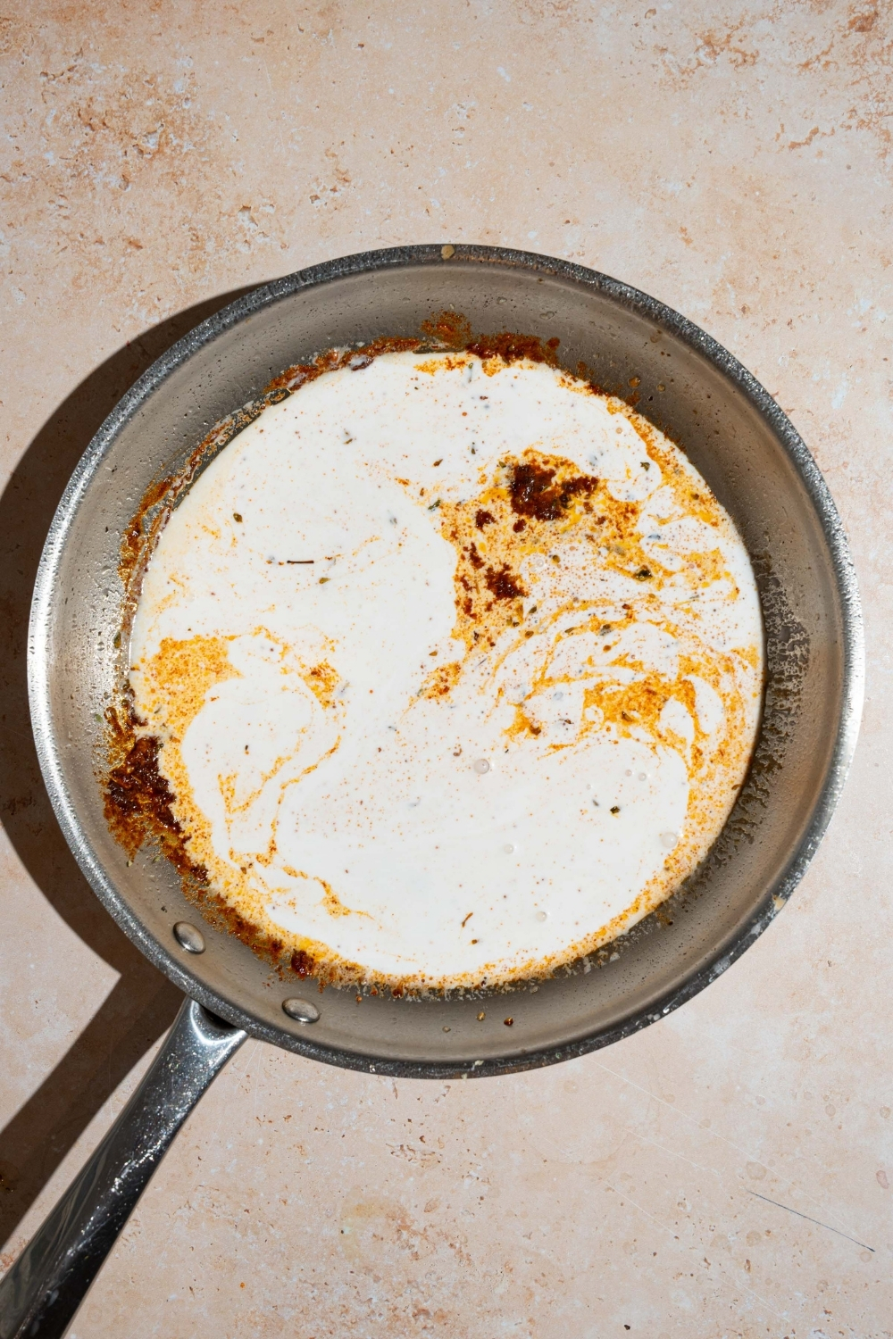 A skillet with garlic and seasonings cooking in heavy cream. The skillet is on tan counter.