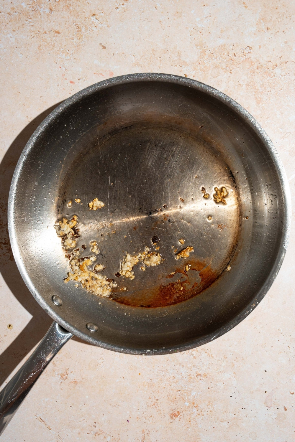 A skillet with garlic cooking in butter. The skillet is on a tan counter.