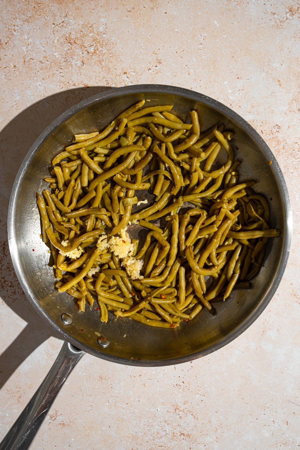 A skillet with canned green beans cooking in butter, garlic, and seasonings.