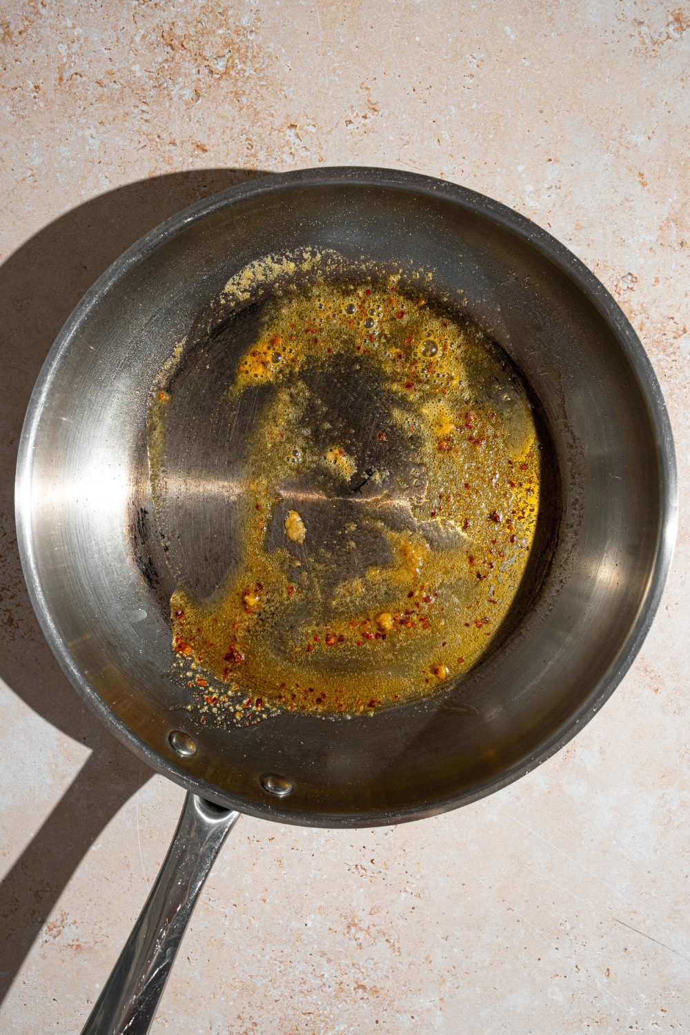 A skillet with melted butter mixed with seasonings. The skillet is on a tan counter.