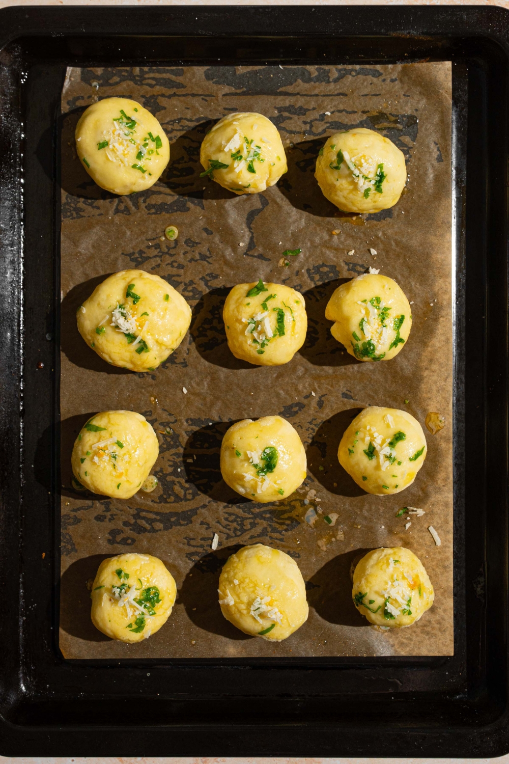 A baking sheet lined with parchment paper with uncooked garlic parmesan cheeseburger bites topped with melted butter.