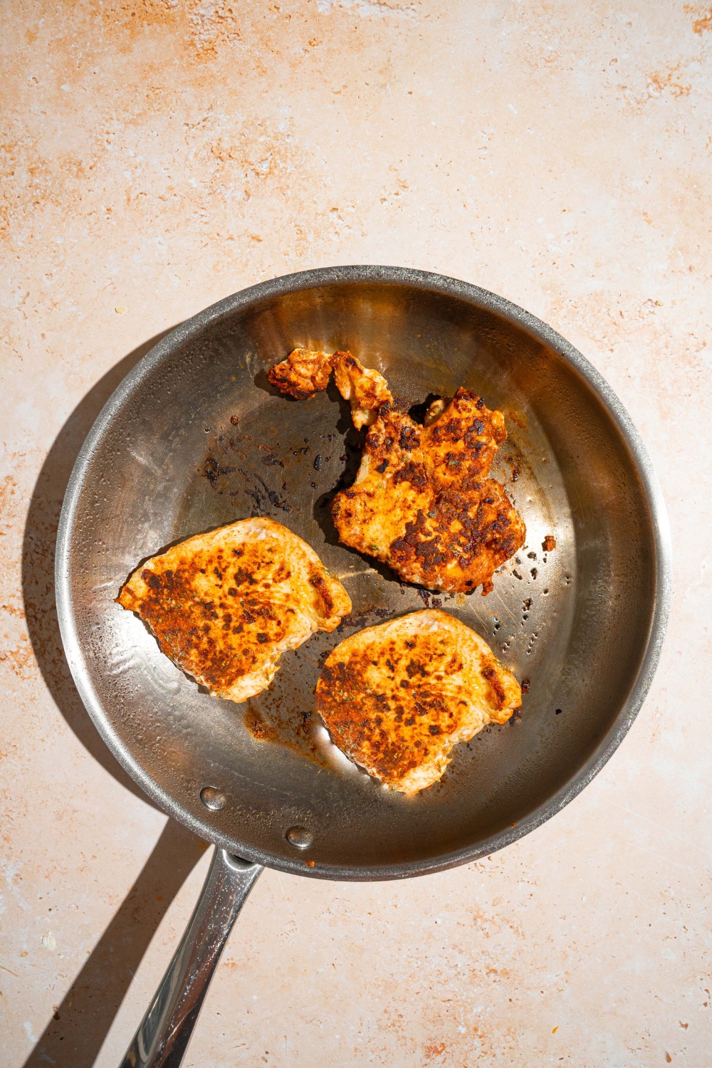 A skillet with sautéed seasoned chicken. The skillet is on a tan counter.