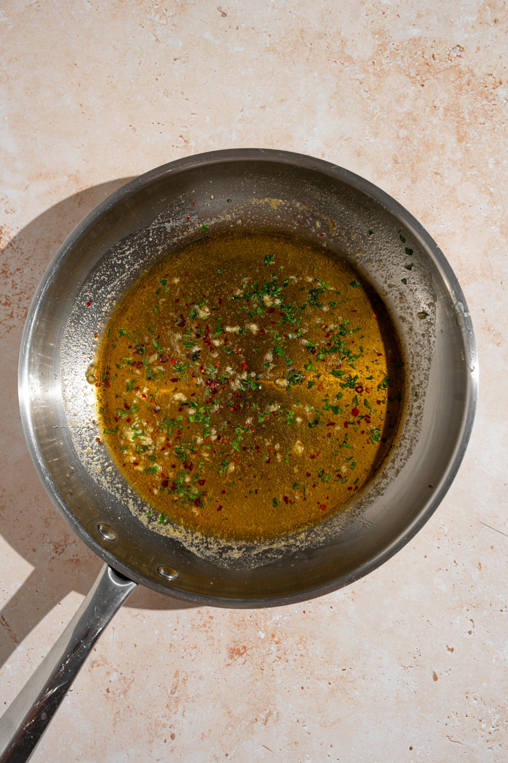 A skillet with melted butter, garlic, and seasonings. The skillet is on a tan counter.
