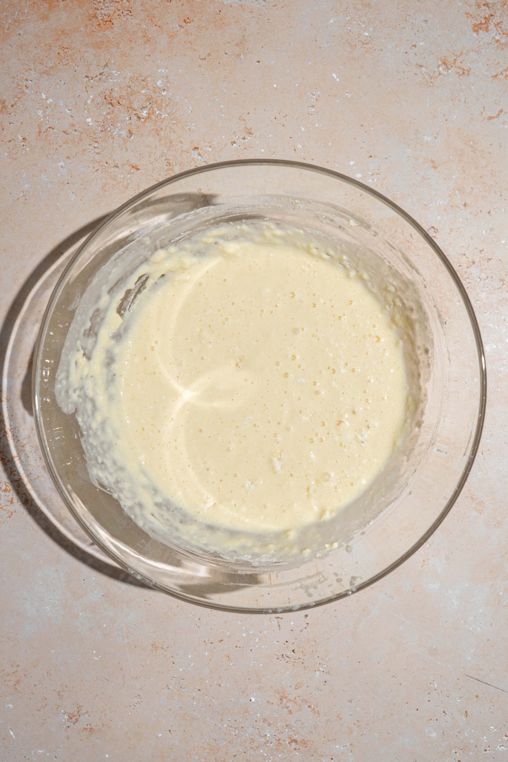 A glass bowl with pancake batter mixture. The bowl is on a tan counter.