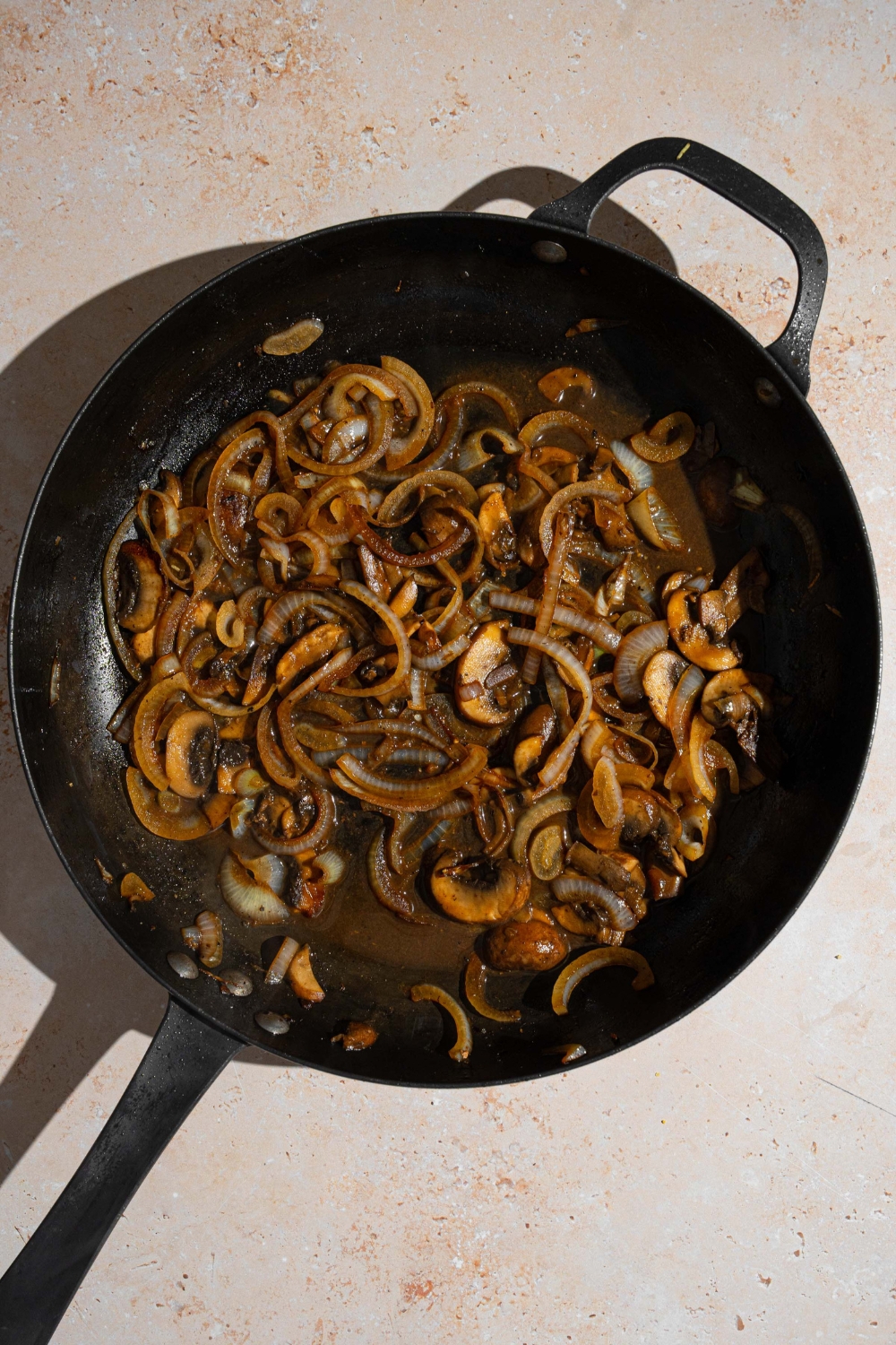 A cast iron skillet with roasted vegetables cooking in oil and seasonings. The skillet is on a tan counter.