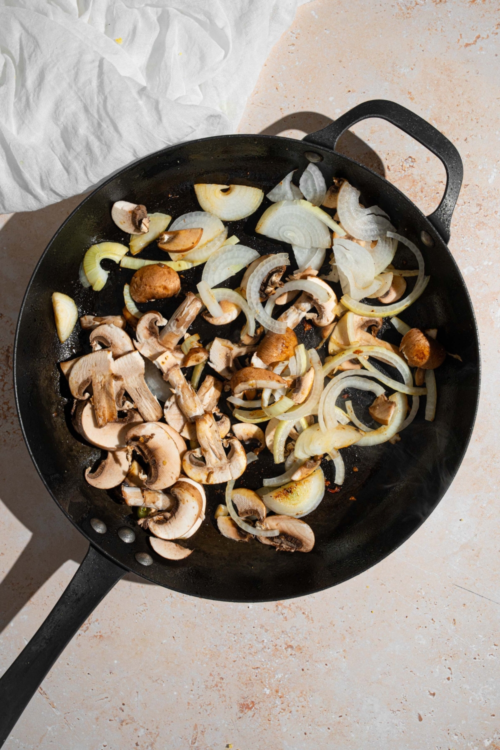 A cast iron skillet with mushrooms and sliced onion cooking in oil.