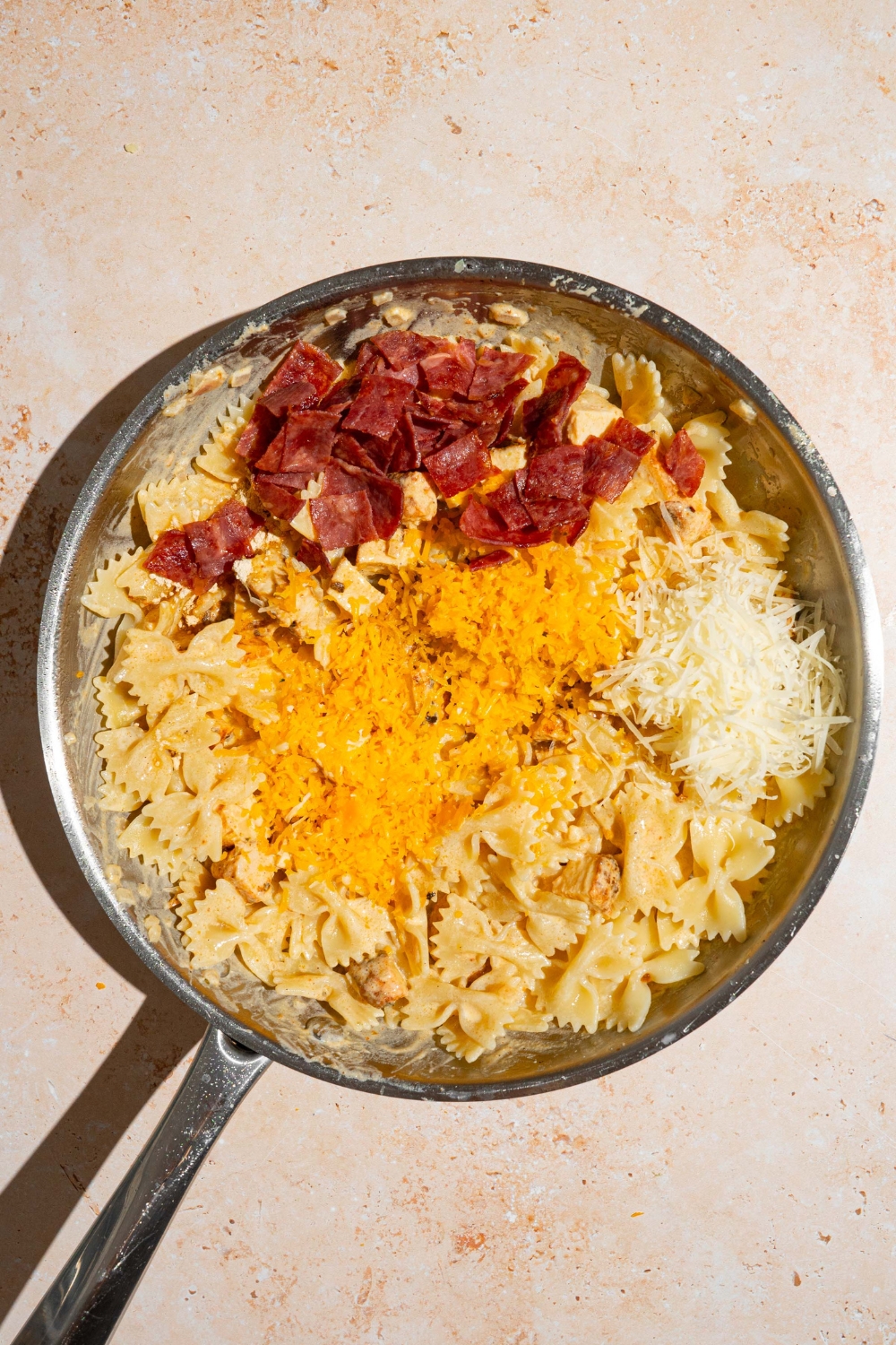 A skillet with cooked pasta topped with chopped bacon, shredded cheese and tossed in bacon ranch sauce. The skillet is on a tan counter.