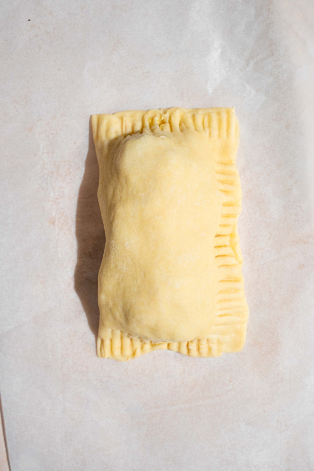 An uncooked wrapped breakfast hand pie on a piece of parchment paper.