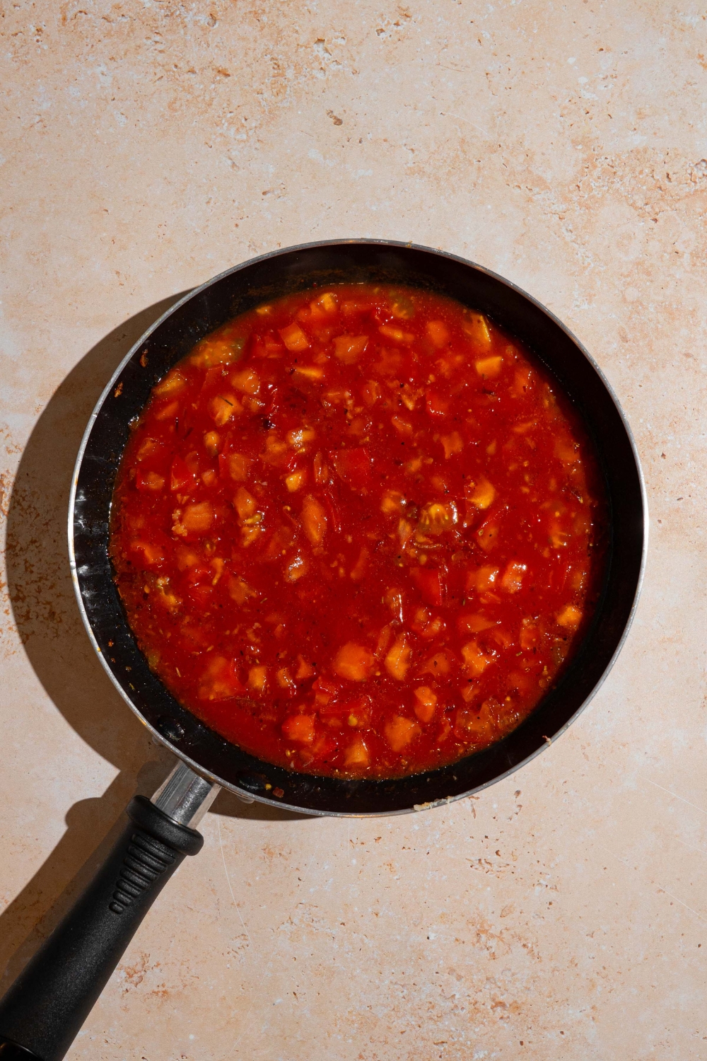 A skillet with cooked tomato sauce. The skillet is on a tan counter.