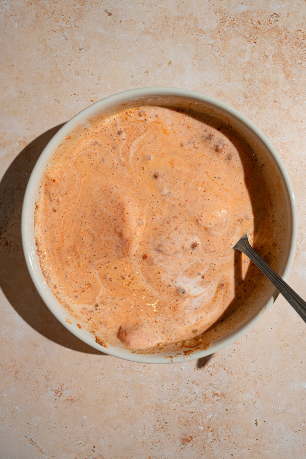 A ceramic bowl with chicken breasts submerged in a buttermilk and hot sauce mixture. The bowl is on a tan counter.