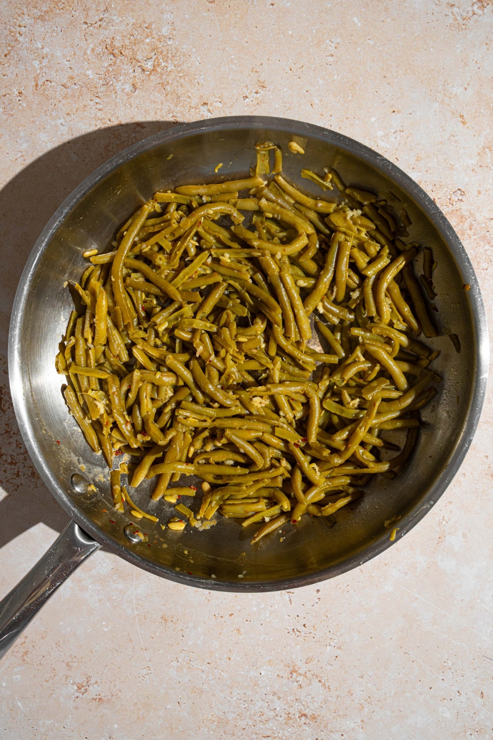 A skillet with canned green beans tossed in garlic butter. The skillet is on a tan counter.