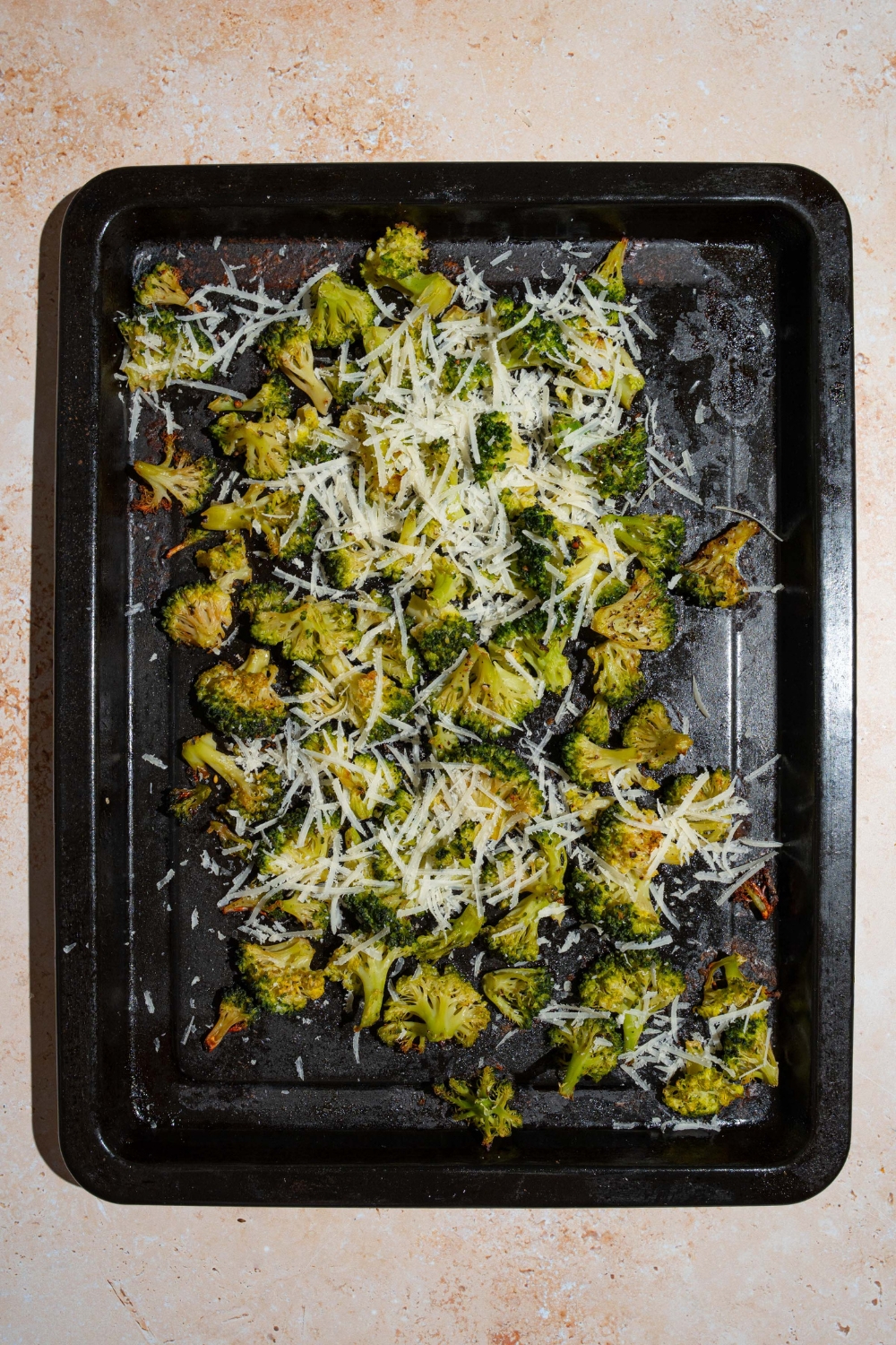 A roasting pan with roasted frozen broccoli topped with grated parmesan. The pan is on a tan counter.