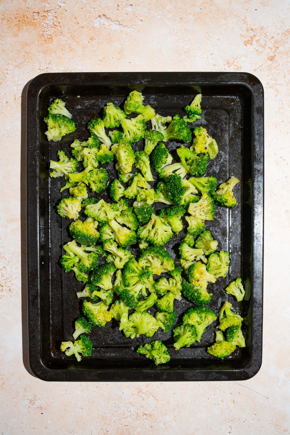 A roasting pan with frozen broccoli. The pan is on a tan counter.