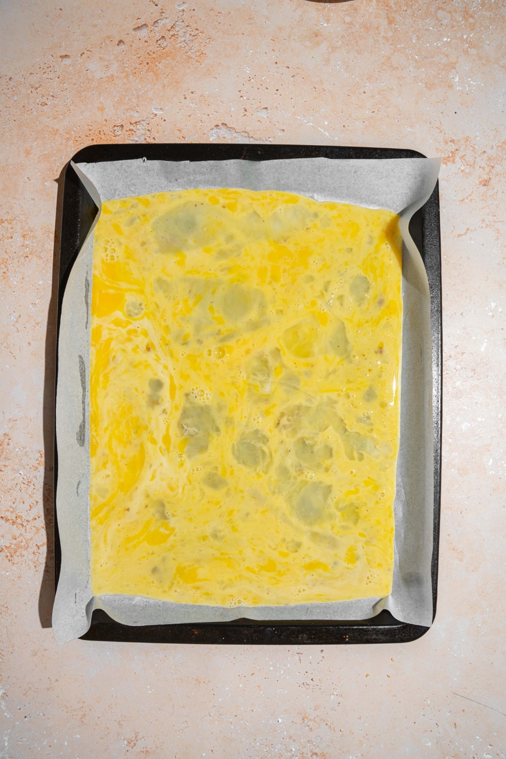 A lined baking sheet with raw egg mixture. The sheet is on a tan counter.
