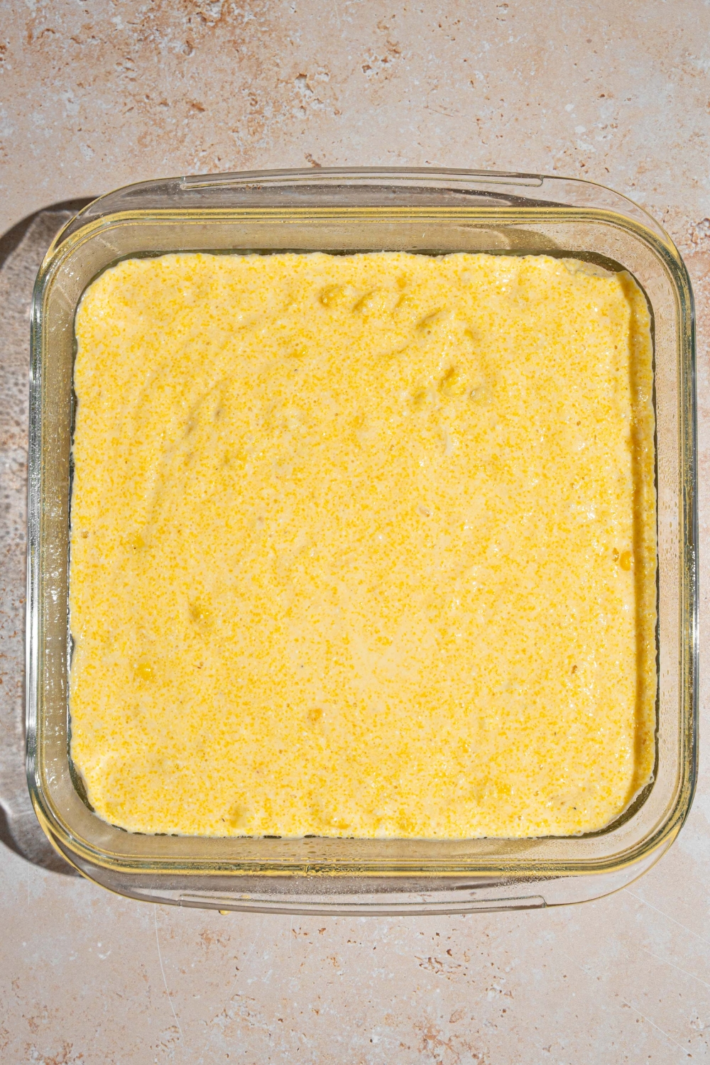 A square glass baking dish with Fat Daddy's cornbread batter. The dish is on a tan counter.