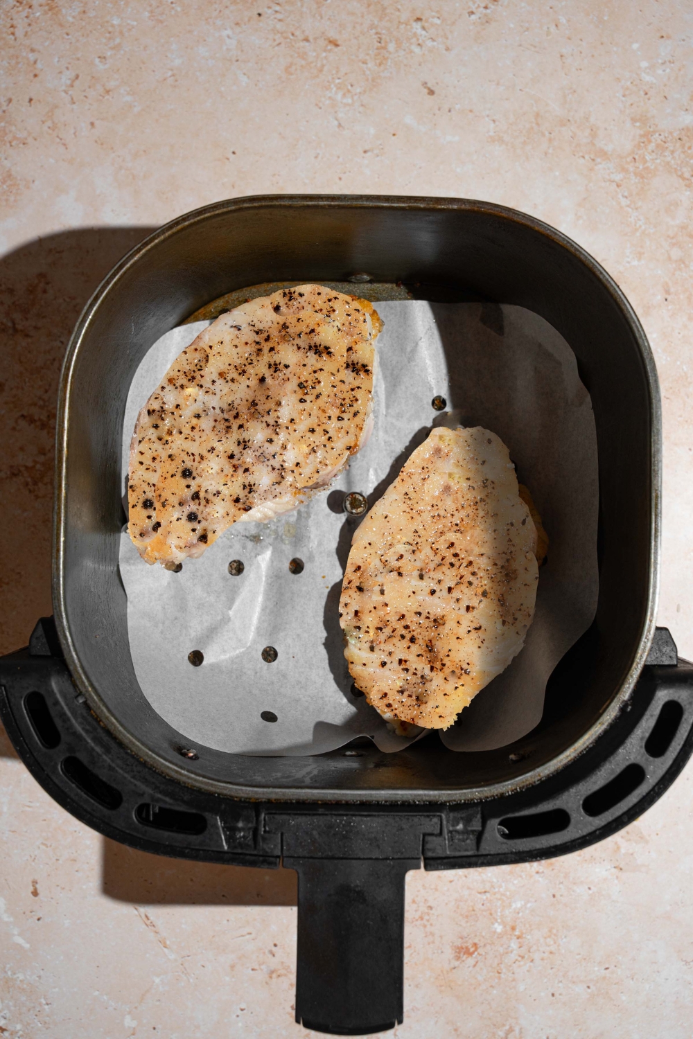 An air fryer with two seared swordfish fillets. The air fryer is on a tan counter.