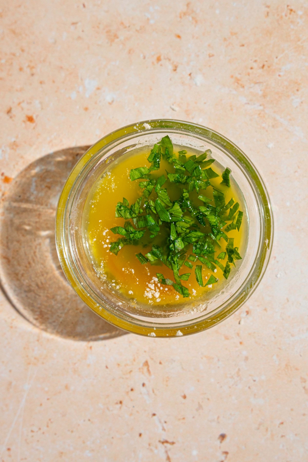 A small glass bowl with melted butter mixture topped with fresh parsley. The bowl is on a tan counter.