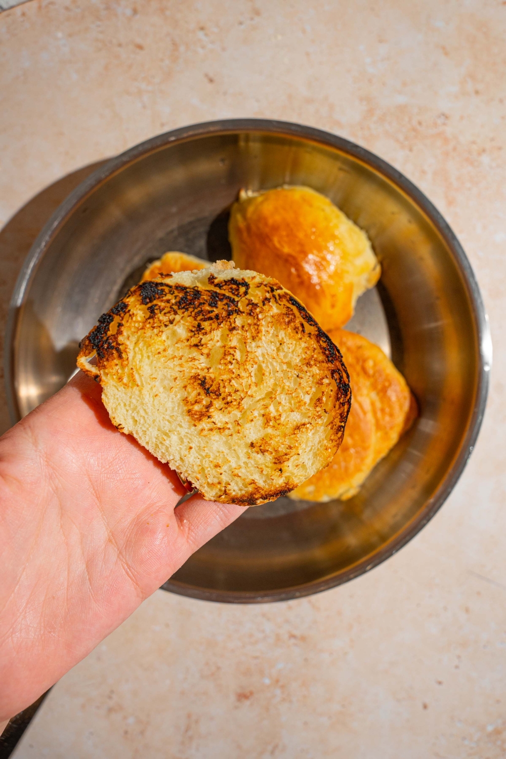 A close up of a hand holding a toasted bun. There is a skillet with buns toasting in butter. The skillet is on a tan counter.