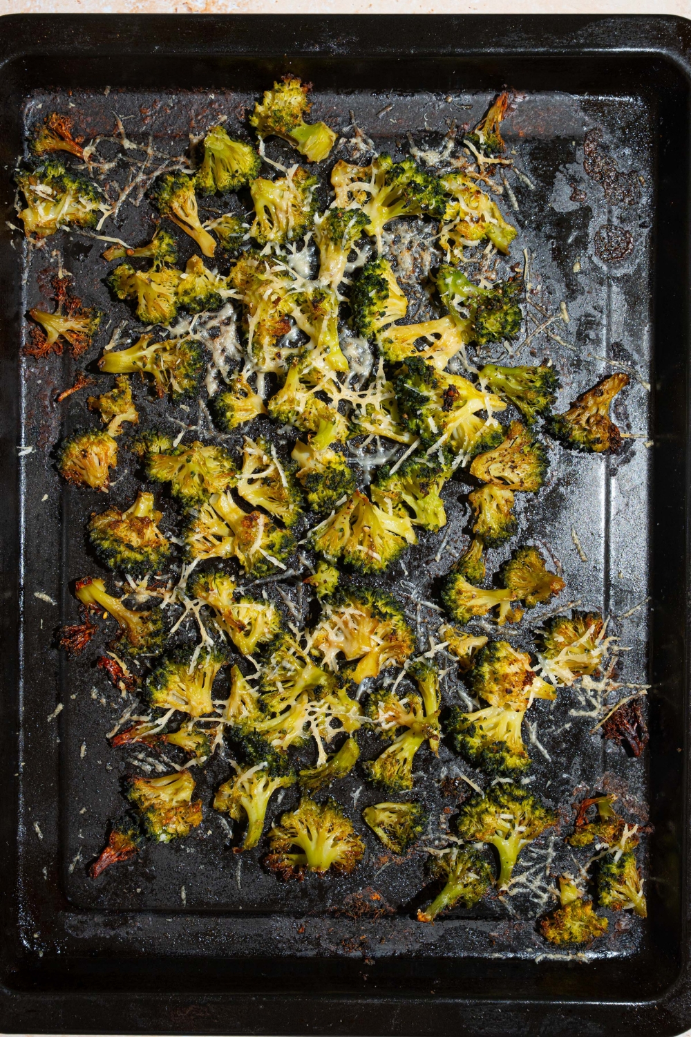 A roasting pan with roasted frozen broccoli topped with grated parmesan.
