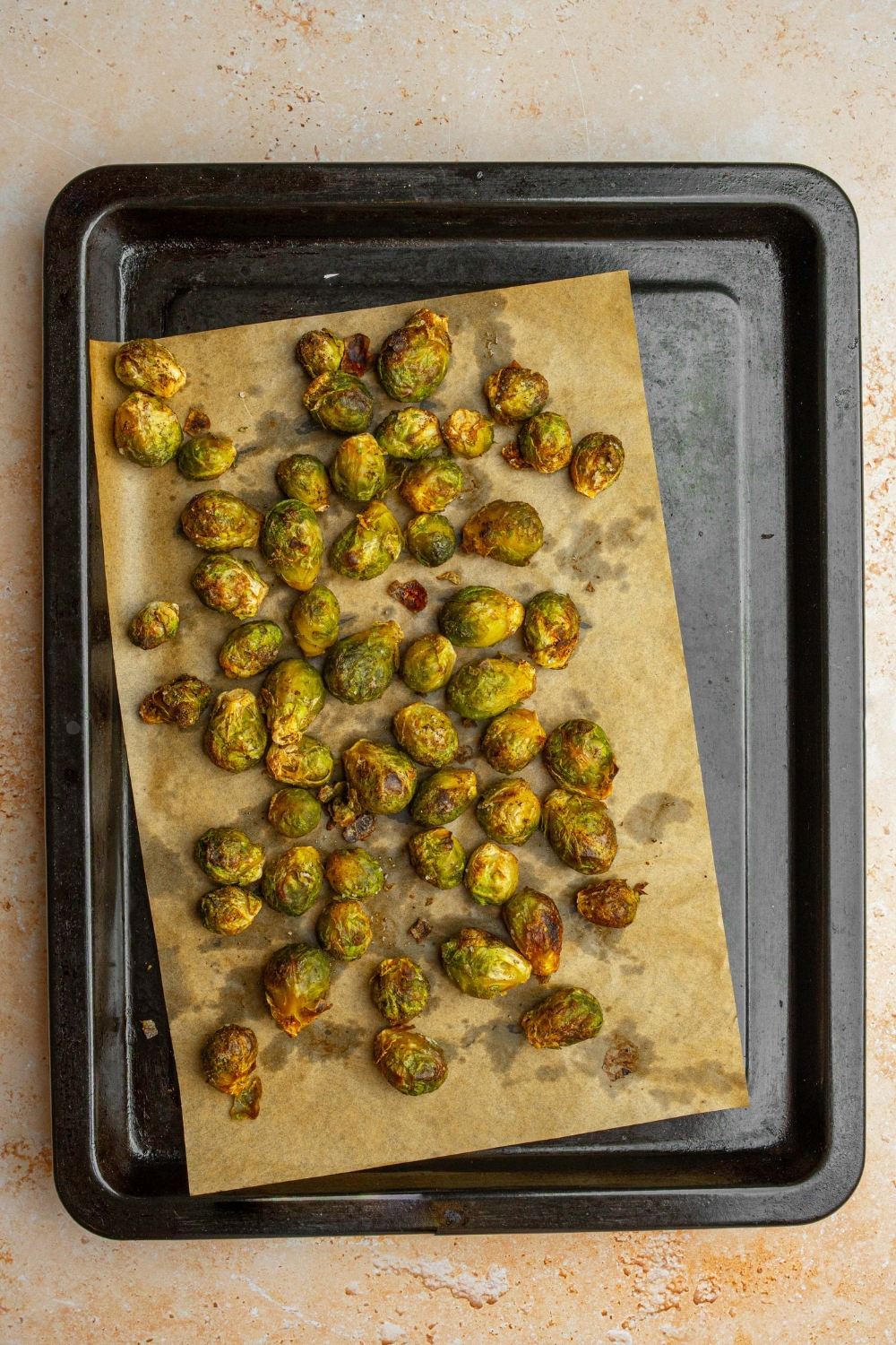 A baking sheet lined with parchment paper with roasted frozen brussel sprouts. The baking sheet is on a tan counter.