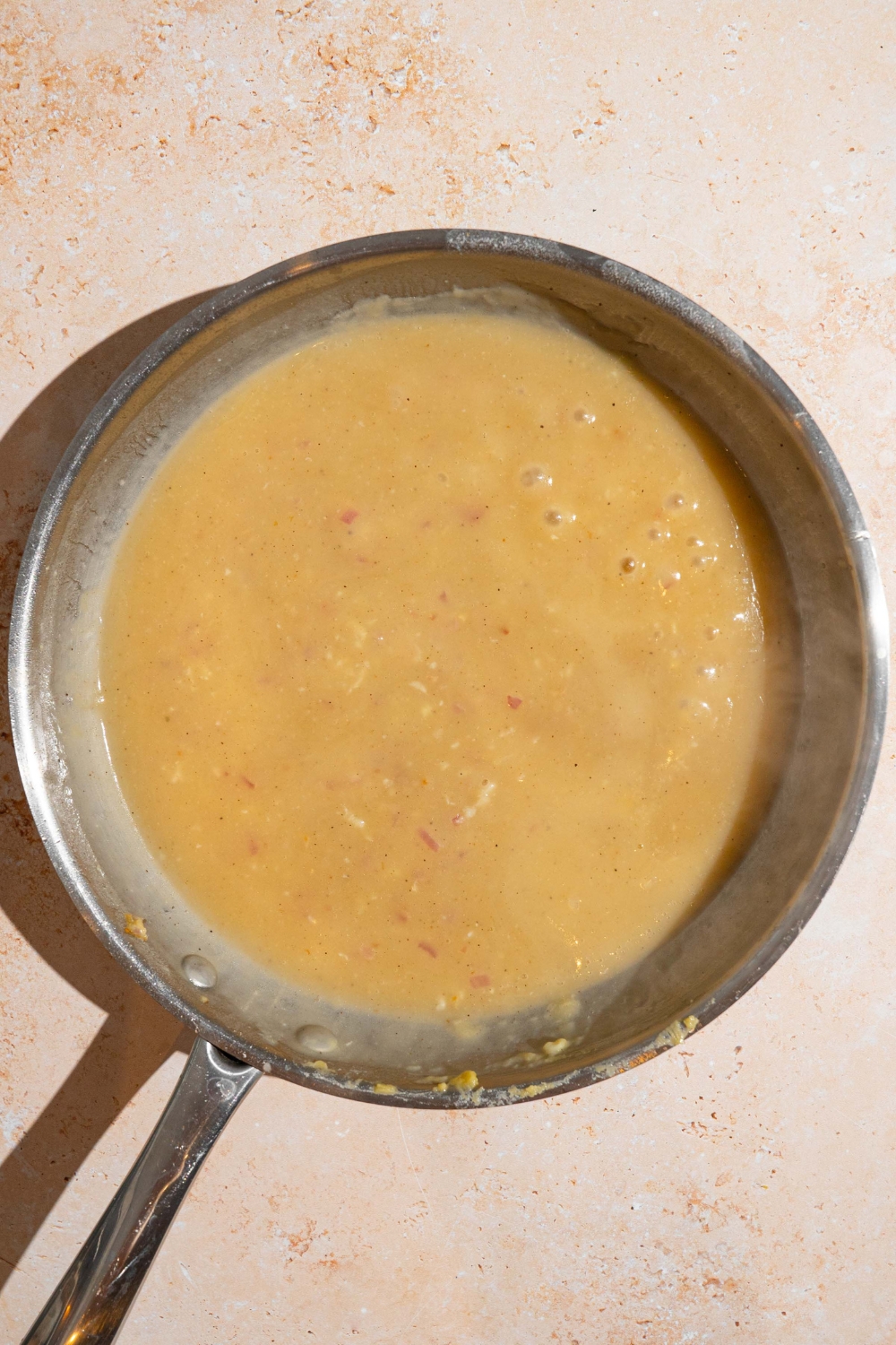 A skillet with a simmering Swedish meatball sauce base. The skillet is on a tan counter.