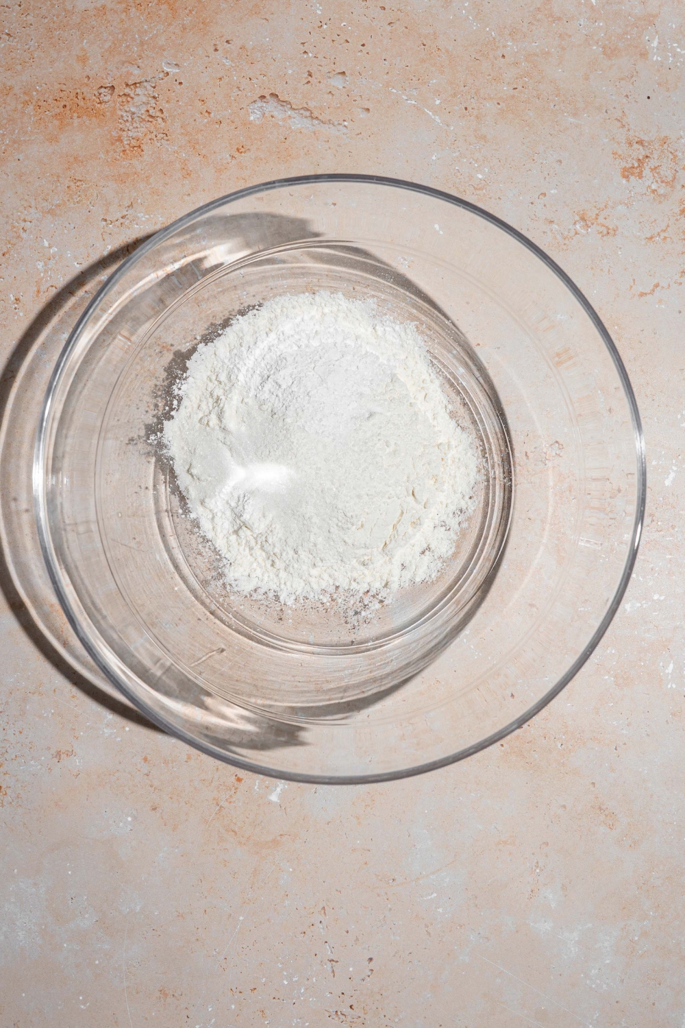 A glass bowl with dry ingredients to make pancakes. The bowl is on a tan counter.