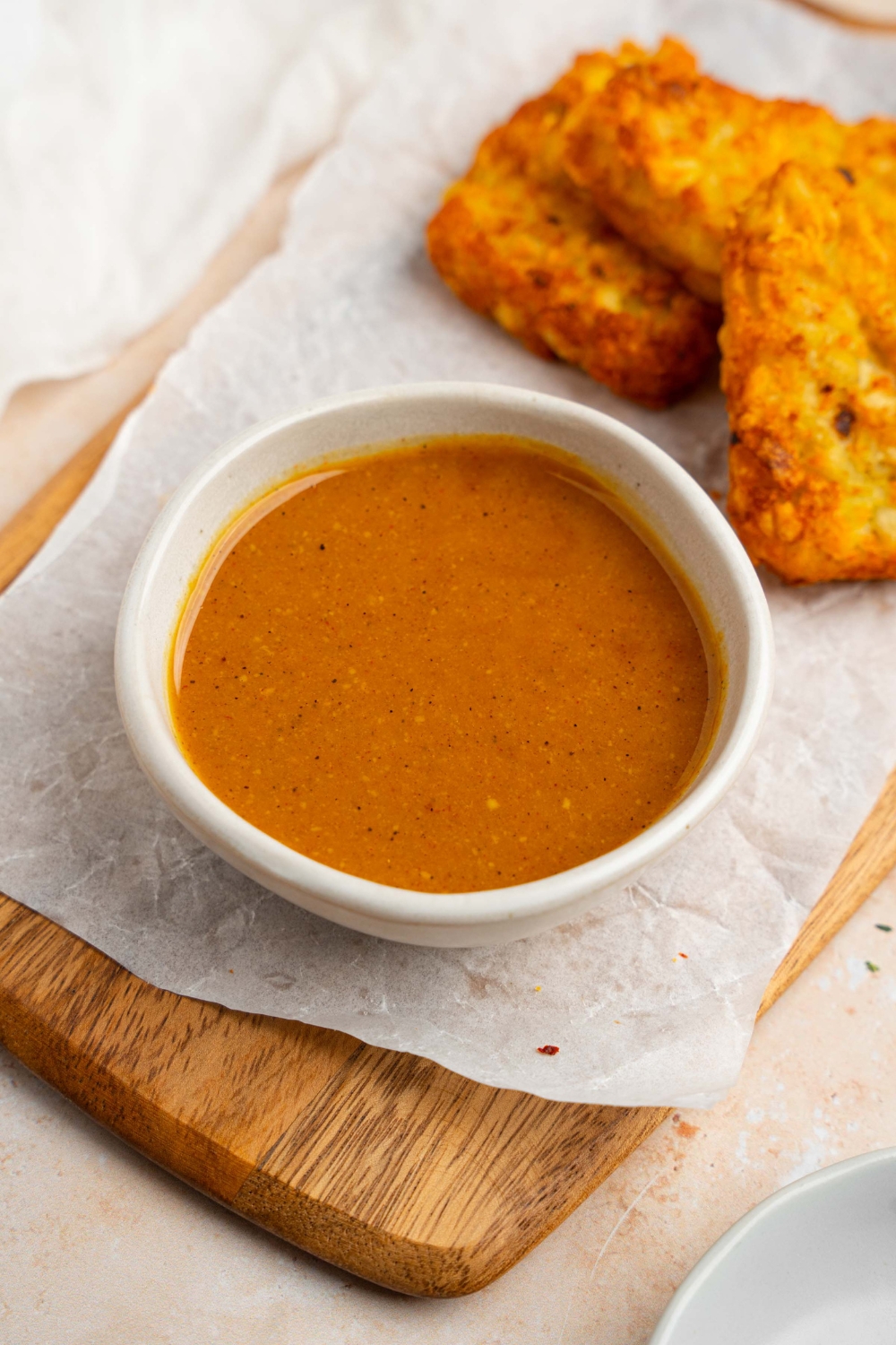 A white bowl of McDonald's golden sauce on a wooden board lined with parchment paper with crispy hashbrowns. The board is on a tan counter with a white cloth napkin.