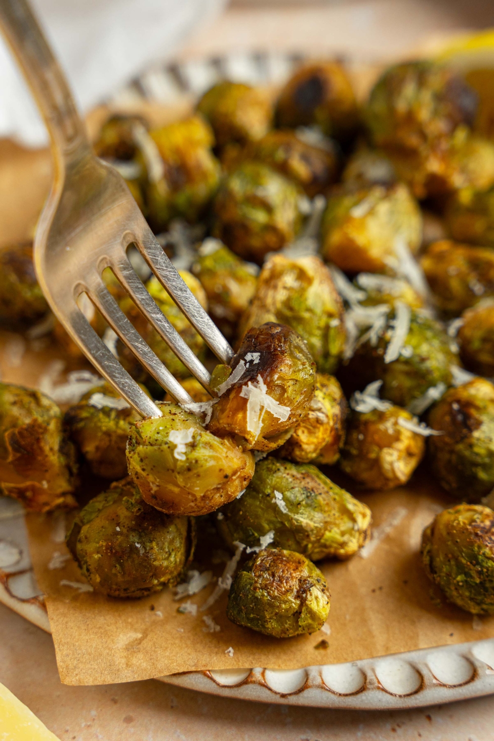 A ceramic plate lined with parchment paper garnished with grated parmesan. There is a fork taking a bite of brussel sprouts.