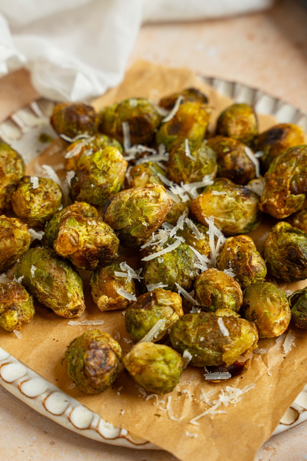 A ceramic plate lined with parchment paper garnished with grated parmesan. The plate is on a tan counter with a white cloth napkin.
