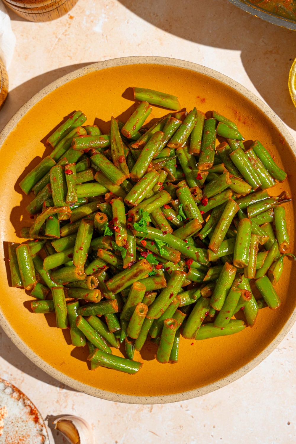 An orange ceramic plate with sautéed frozen green beans tossed in seasonings. The plate is garnished with fresh parsley. The plate is on a tan counter.