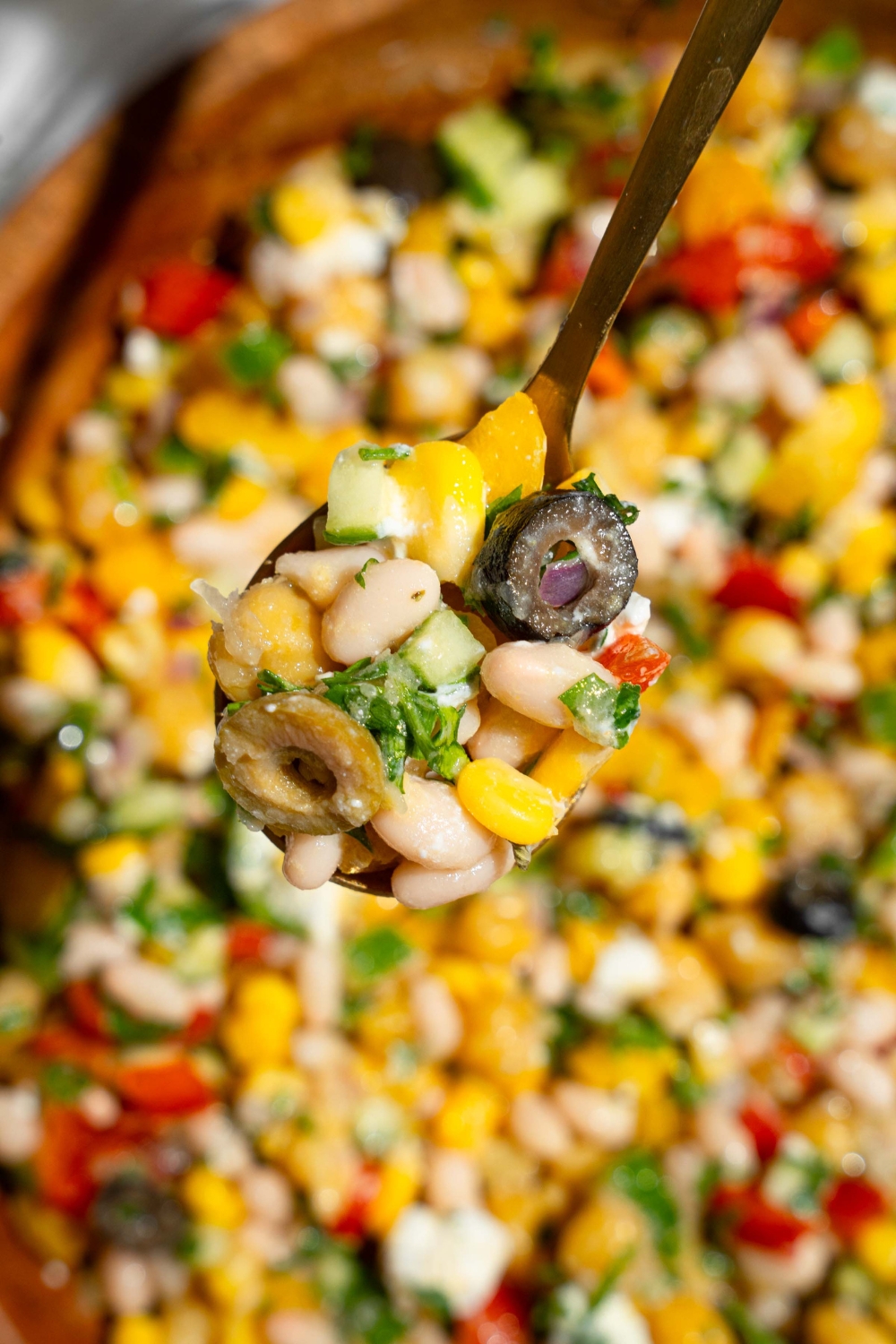 A close up of a spoon with a bite of dense bean salad garnished with fresh parsley. There is a bowl of bean salad blurred in the background.